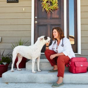 Dr. Angie O'Hearn sits with a white dog near a front door.